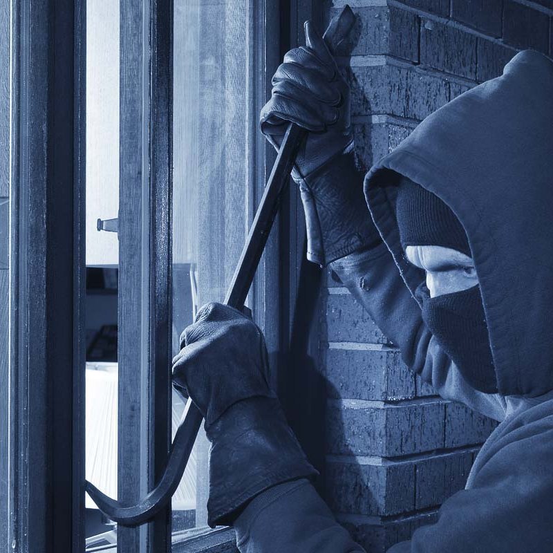 Ein Einbrecher der ein Fenster mit einer Brechstange öffnet